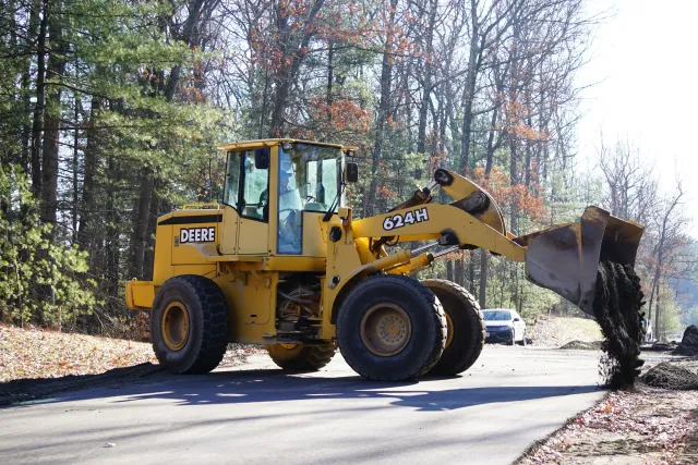 A yellow John Deere front loader bulldozer moving dirt in a wooded area during daytime.