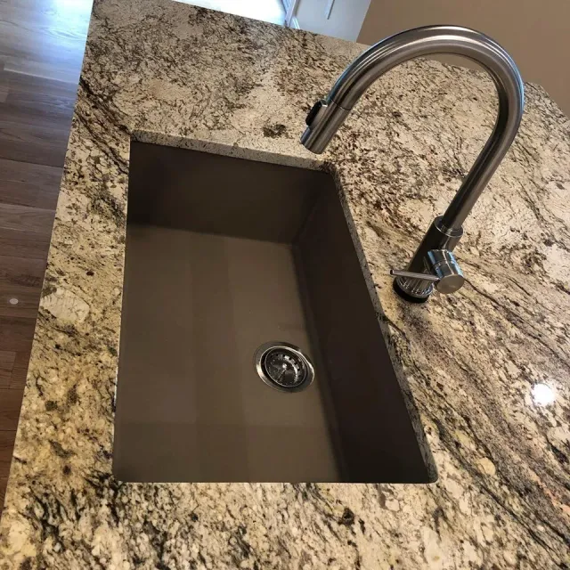 A kitchen sink with a faucet on a granite counter top