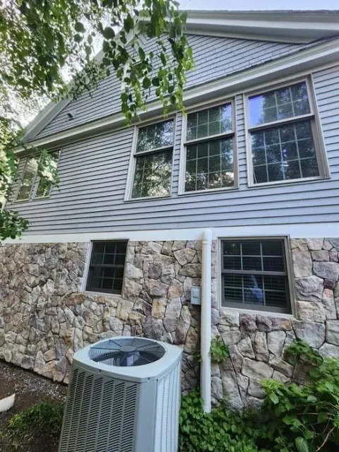 House exterior with stone lower facade, gray siding, windows, and a central air conditioner unit in front