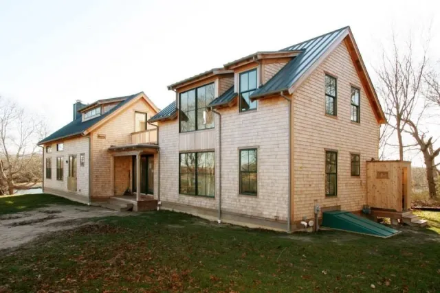 New two-story house with large windows, unfinished porch, and a small attached shed on a grassy lot.