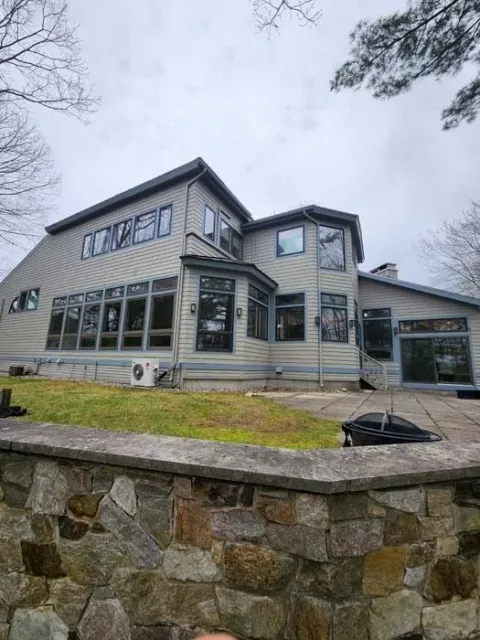 Large gray house with many windows behind a stone retaining wall under an overcast sky