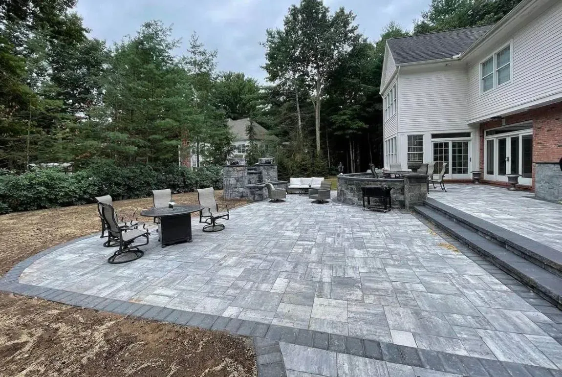 Stone patio with a fire pit, curved path, and lush garden trees under a bright blue sky