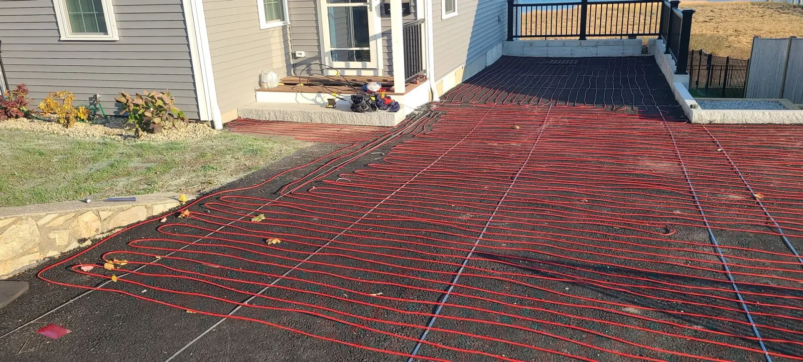 Red mesh tarp covering a sloped driveway beside a house entrance and porch steps.