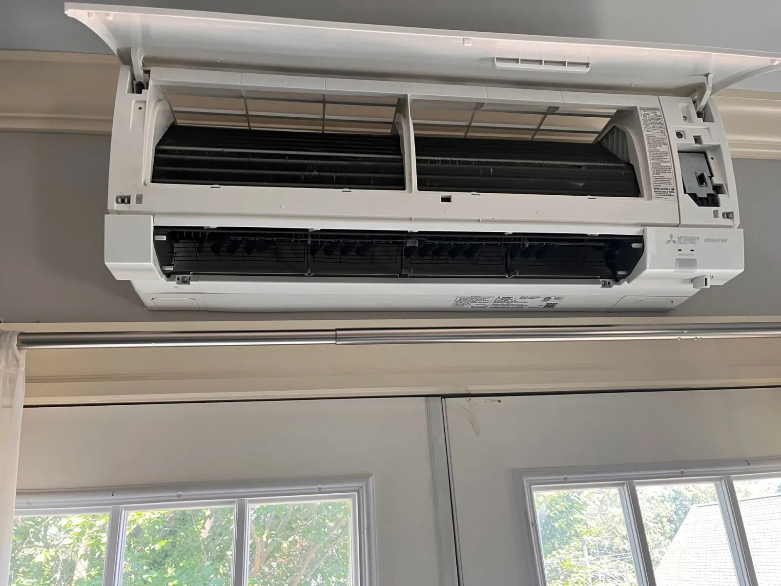 A white air conditioner is hanging from the ceiling in a room next to a window.