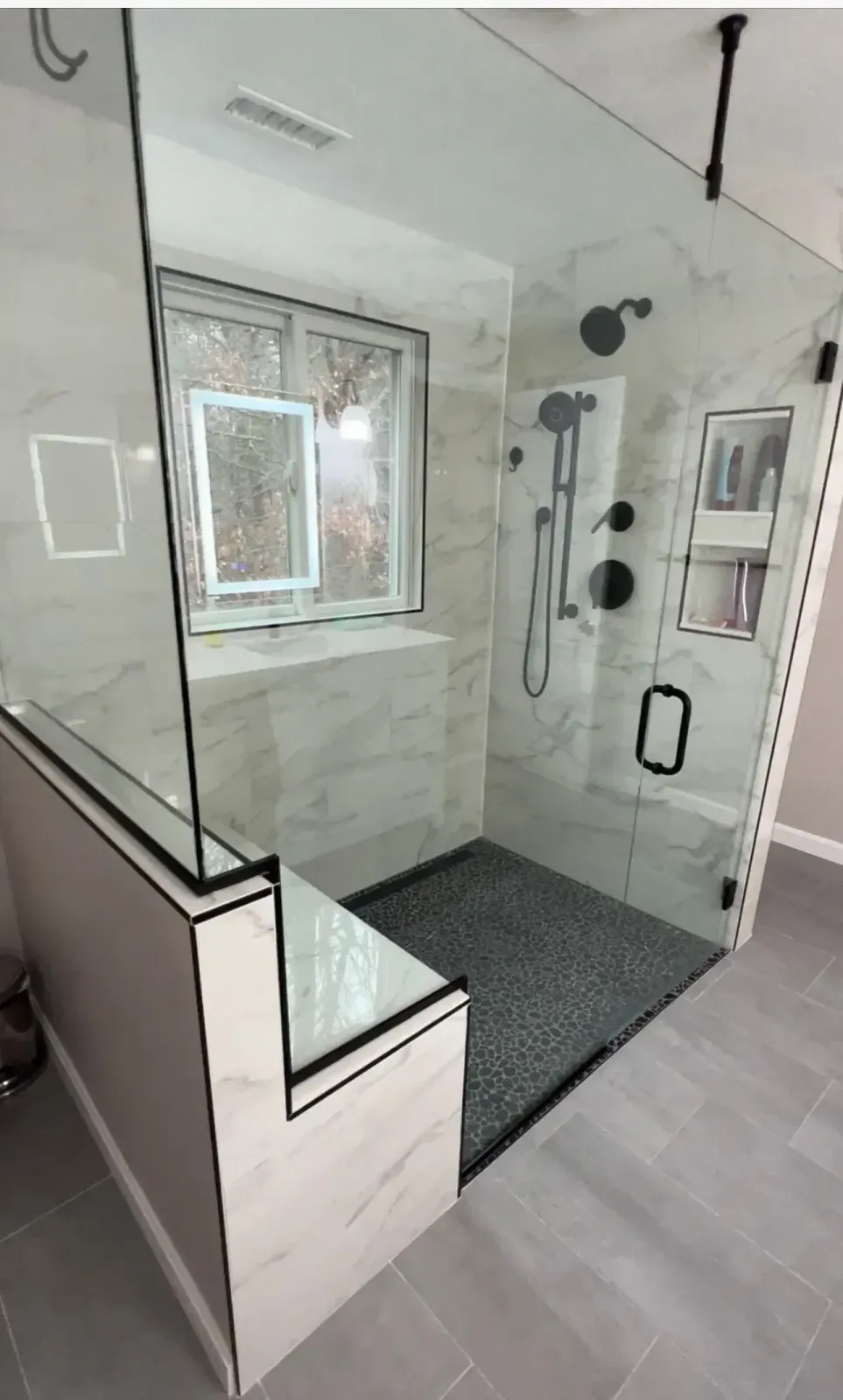 Modern white bathroom with glass shower enclosure, tiled walls, window, and dark bath mat