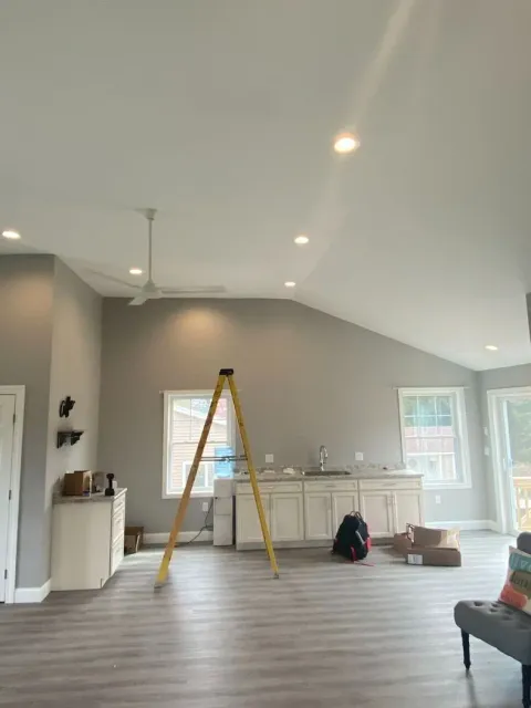 Bright living room with sloped white ceiling, gray walls, ladder, and cabinets under windows