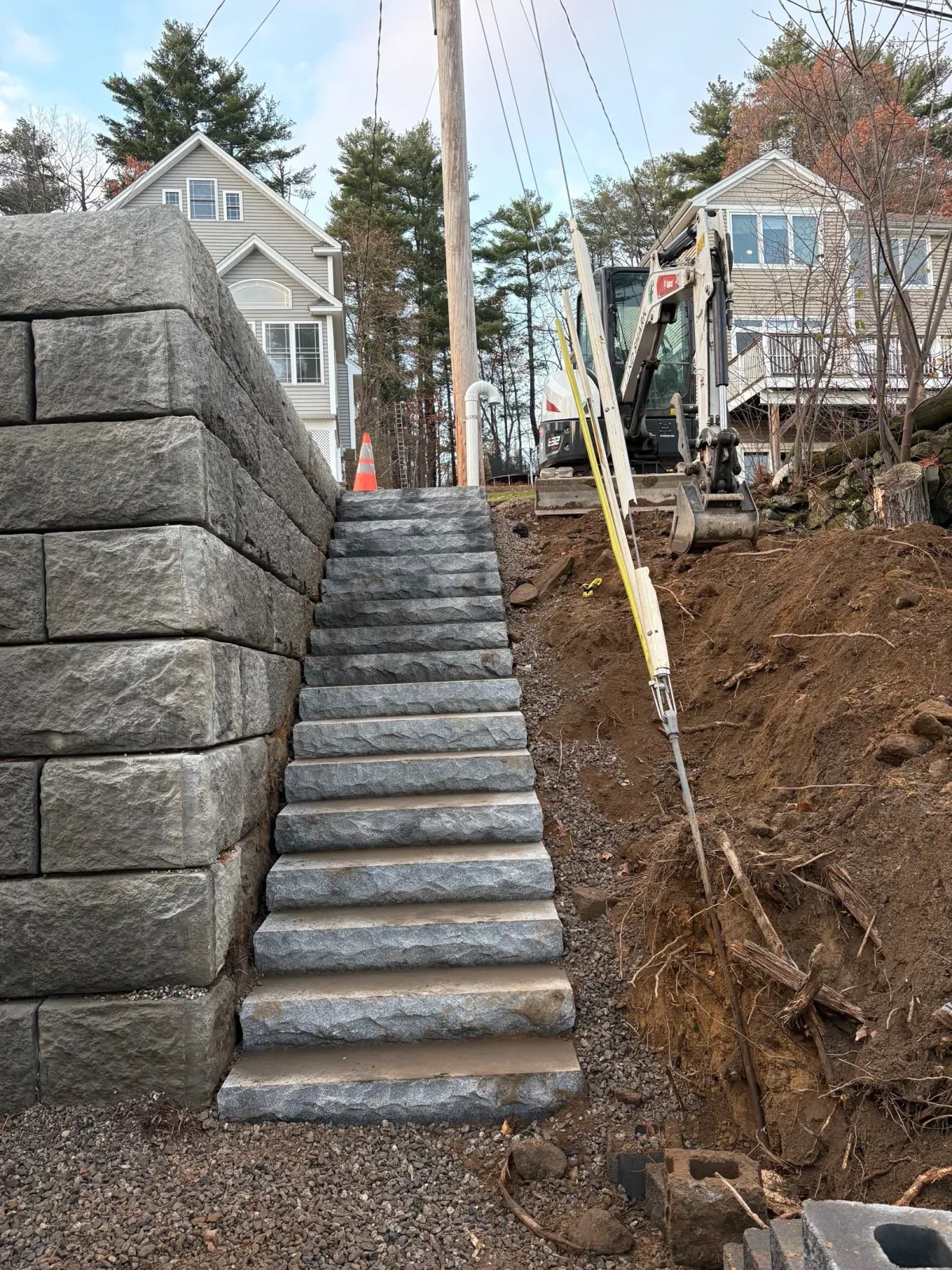 Stone staircase built alongside a retaining wall and dirt embankment, leading uphill between two houses.