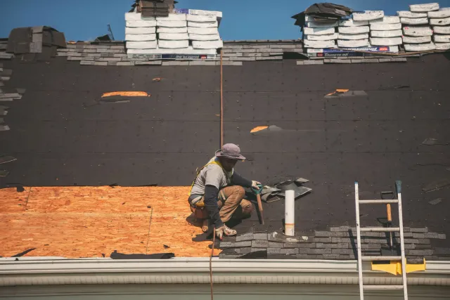 Worker installing shingles on roof under construction.