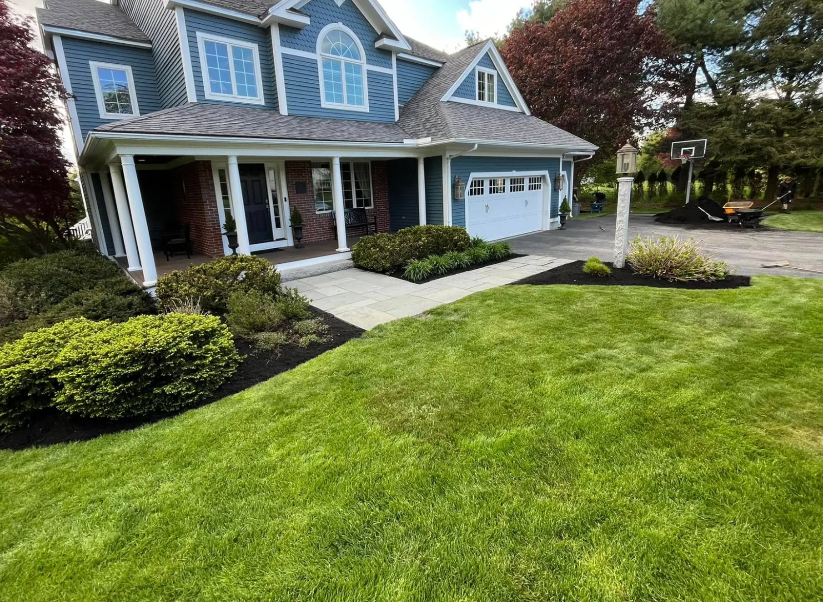 Newly landscaped front yard with freshly cut green grass, landscaped bushes, a paved walkway, and a house with blue siding, white trim, and a two-car garage.