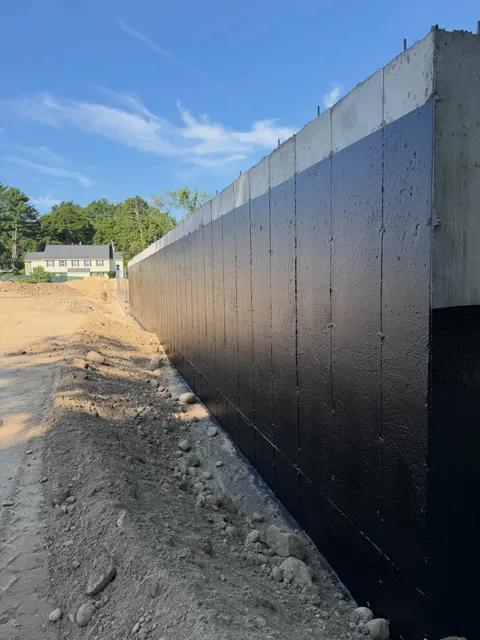 Long foundation wall coated in black waterproofing membrane before backfill
