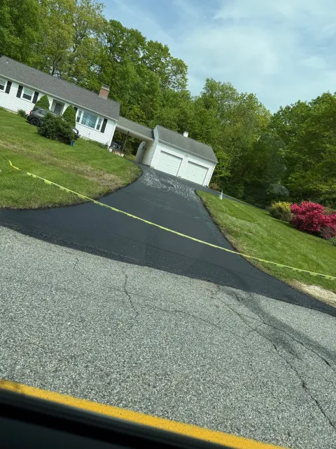 Tilted view of a suburban driveway leading to a white house and garage, with trees and grass along the sides