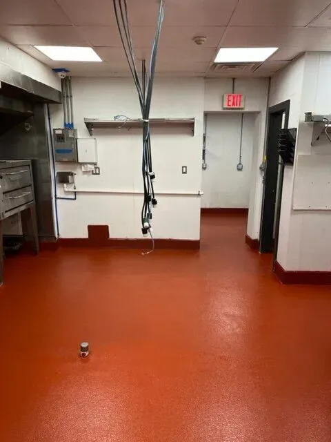 An empty kitchen with a red floor and a red exit sign