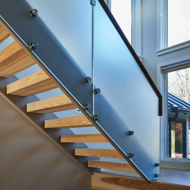 Architectural detail of a modern staircase with wooden steps, glass railing, and metal fasteners.