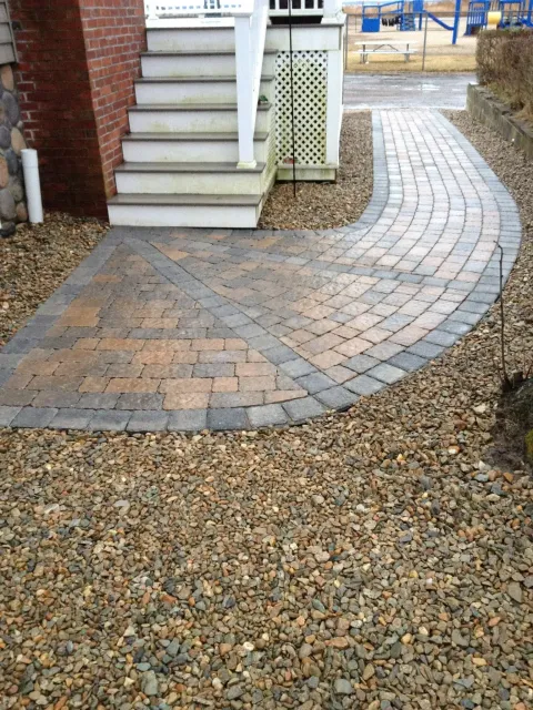 A brick walkway leading to a house with stairs