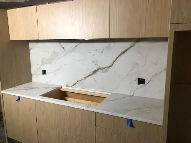Kitchen remodel: Light wood cabinets, marble backsplash and countertop, unfinished sink cutout, black outlets.
