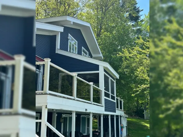 Blue house with white balconies and trim surrounded by green trees on a sunny day