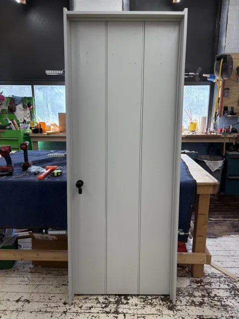 A white metal cabinet with four doors, placed on a workbench in a workshop with tools and supplies in the background.