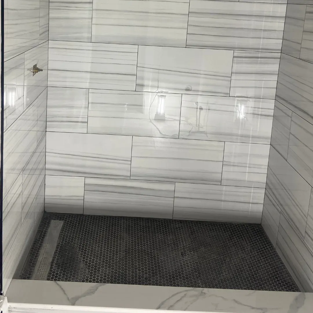 Walk-in shower with white veined marble large-format tile and dark hex mosaic floor by SF Construction in Southborough, MA