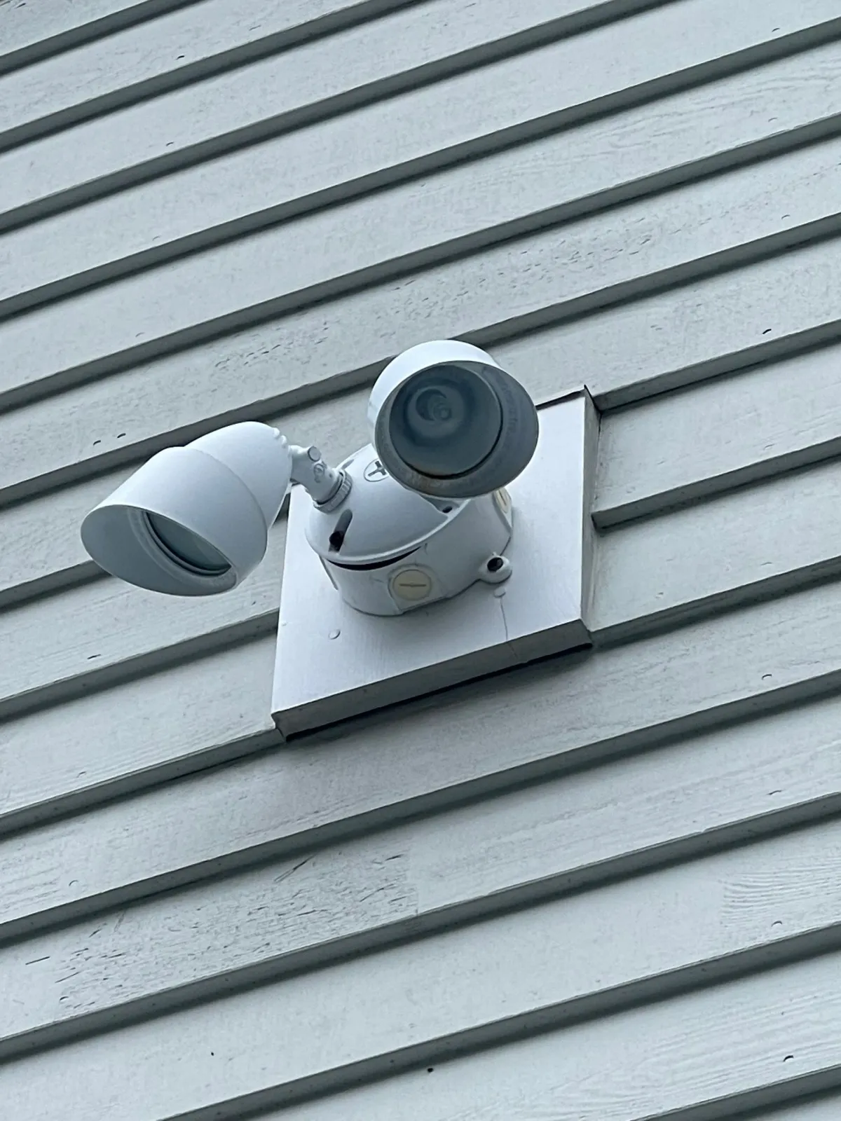 White outdoor security light mounted on white siding.