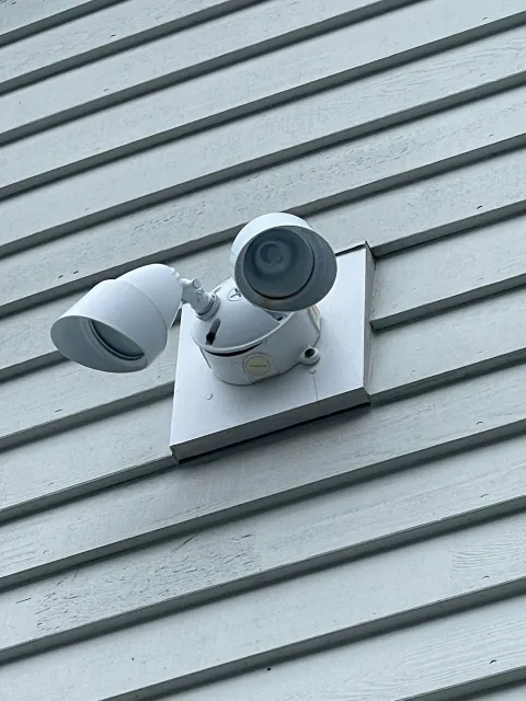 White outdoor security light mounted on white siding.