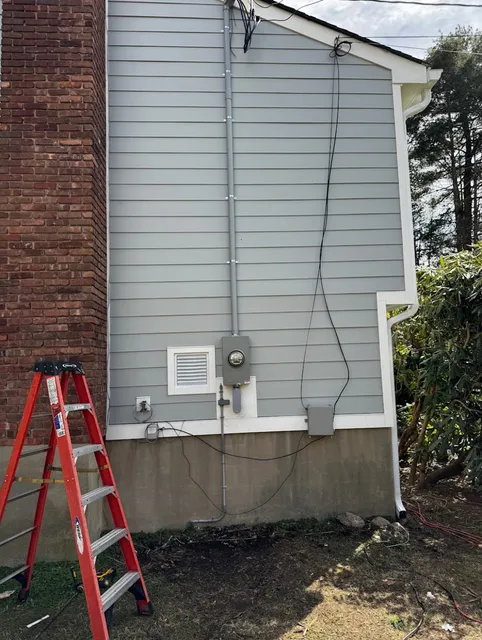 Electrical Meter and Wiring Installation on the Exterior Wall of a House with a Ladder in Front