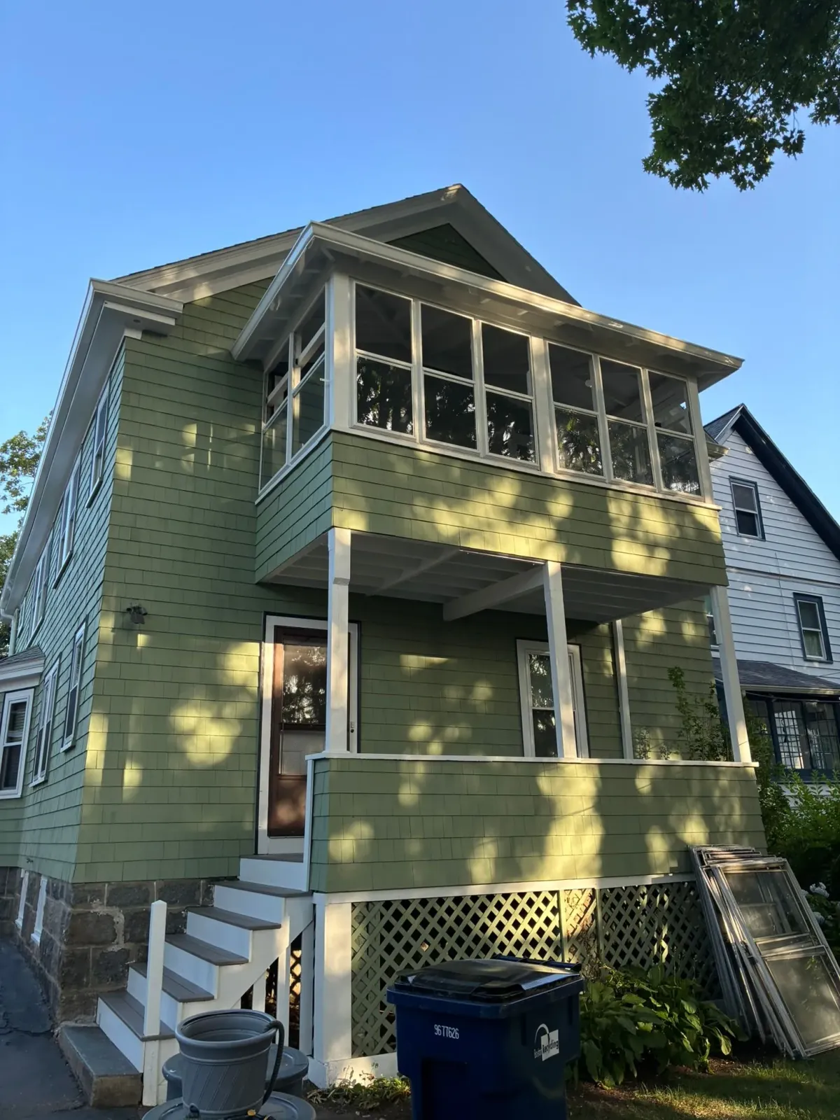 Green two-story house with front porch, stairs, and lattice under a blue sky