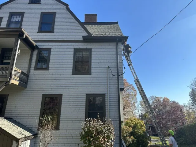 White house exterior with a ladder leaning to the roof under a clear blue sky