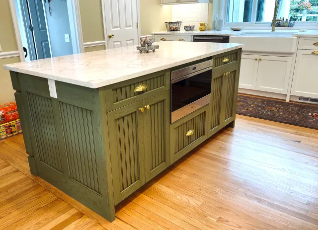 a kitchen island with green cabinets, a built-in oven, and a marble counter top