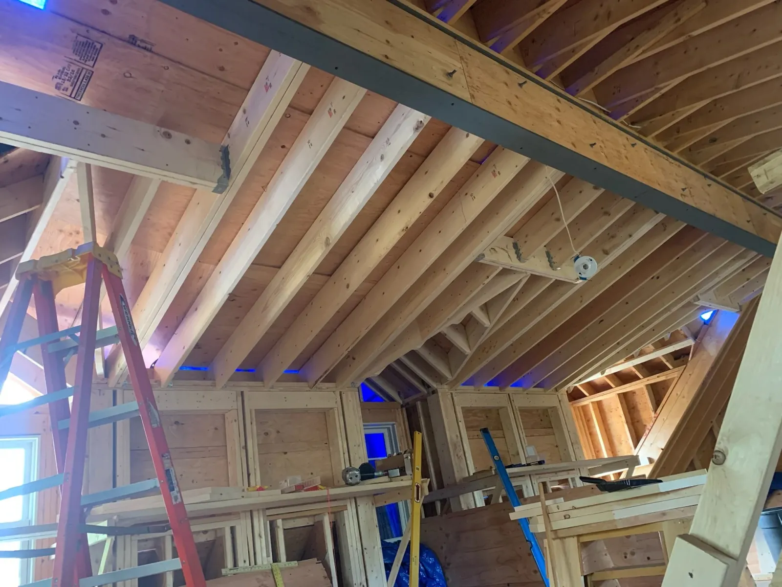 Interior of a house under construction, showing wooden framing and ceiling joists with ladders and construction tools. Scituate, Norwell, Hanover, Hanson, Marshfield, South Shore. Massachusetts Local Construction Company.