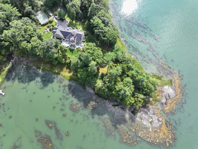 Aerial view of a house on a lush green peninsula with coastal water