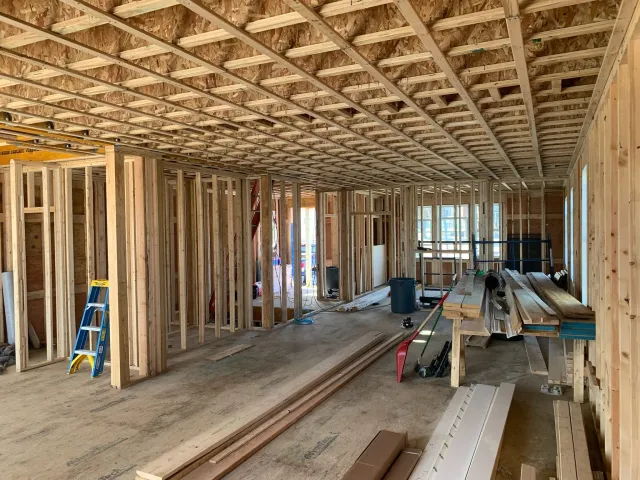 Interior of a house under construction with exposed wooden framing, no drywall, construction tools, and materials scattered around. Scituate, Norwell, Hanover, Hanson, Marshfield, South Shore. Massachusetts Local Construction Company.