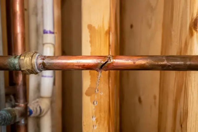 Burst copper pipe leaking inside an exposed wall cavity