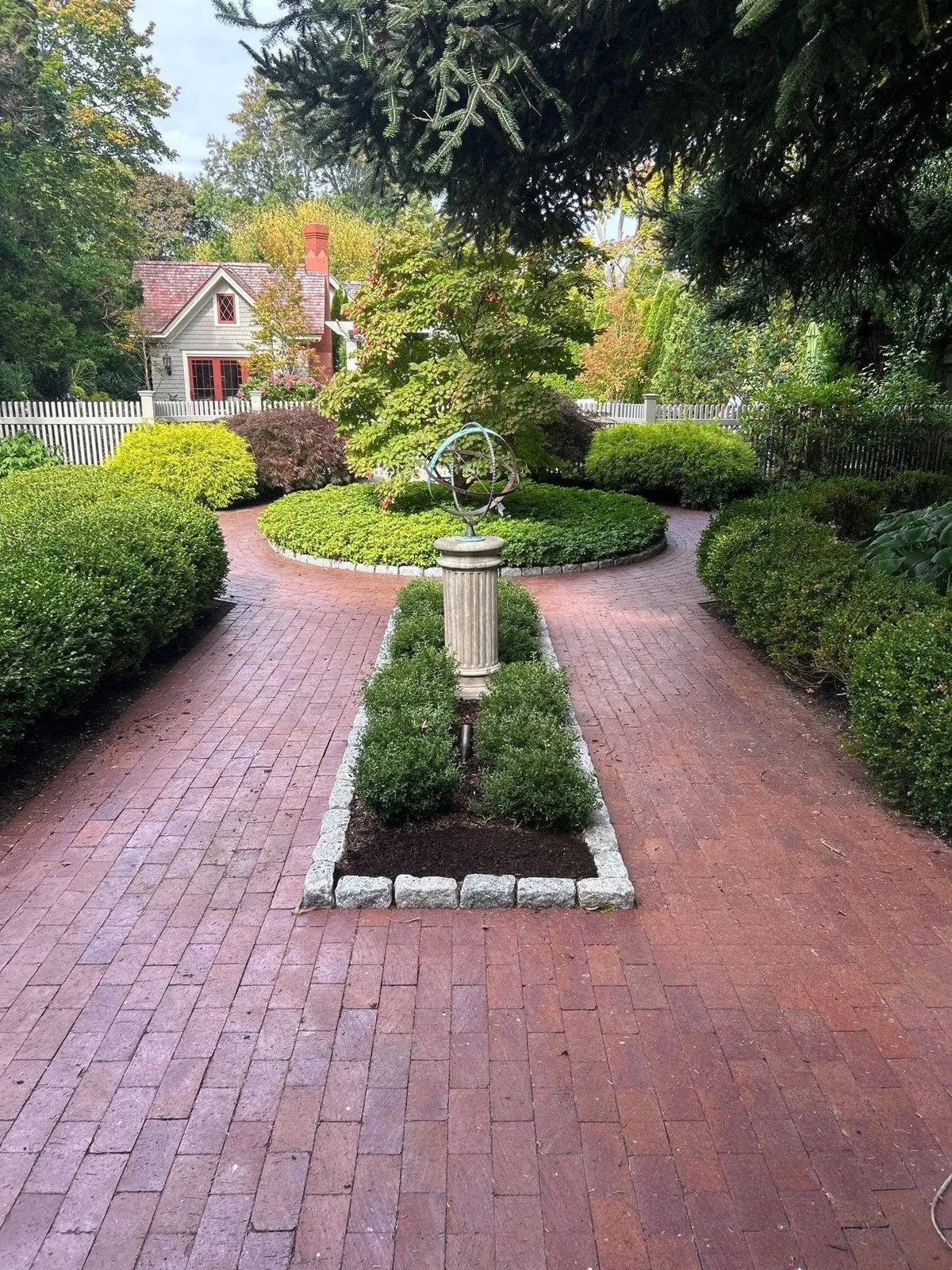 A gorgeous garden with a well-maintained brick path leading to a small home in the background.
