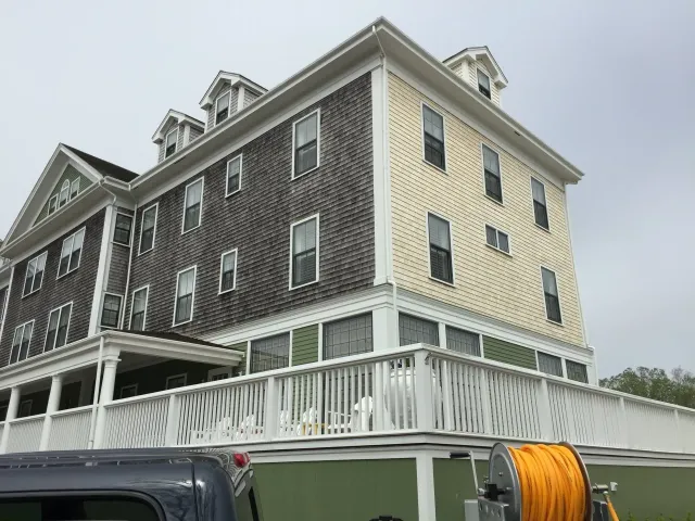 Multi-story building with yellow and gray siding, white trim, and a wrap-around porch.