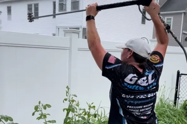Woman power washing a white fence with a multi-nozzle wand. G&L Softwash shirt visible. Pressure washing and softwash home services.