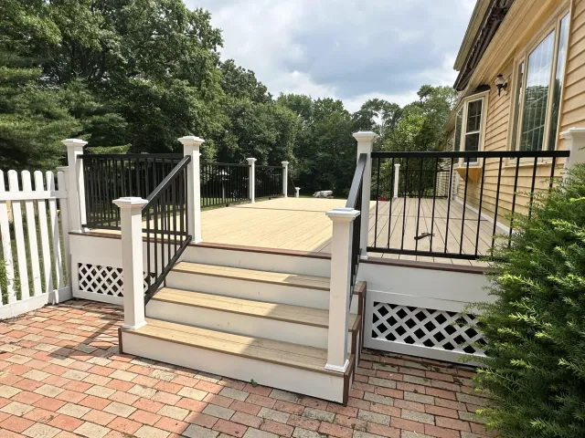 backyard-deck-with-wide-steps-black-railings-and-wooded-view-behind-house.webp
