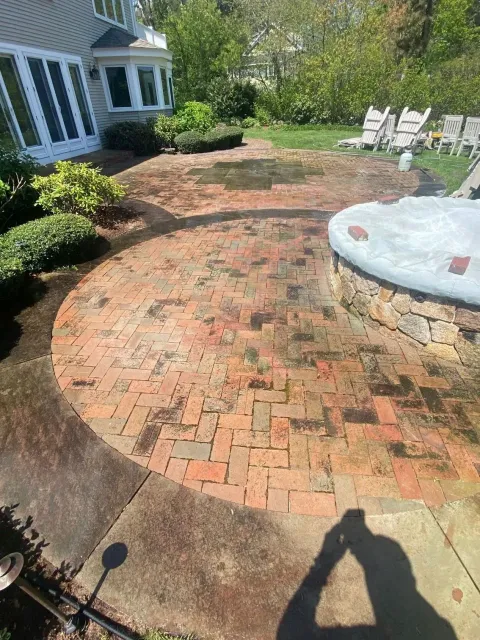 Brick patio with wet spots, adjacent to a house and spa. Person's shadow is visible, taking photo.