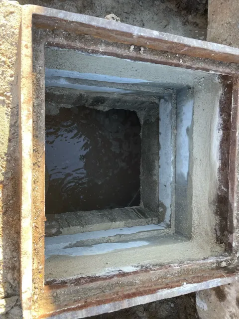 A square hole in the ground with a metal frame surrounding it.
