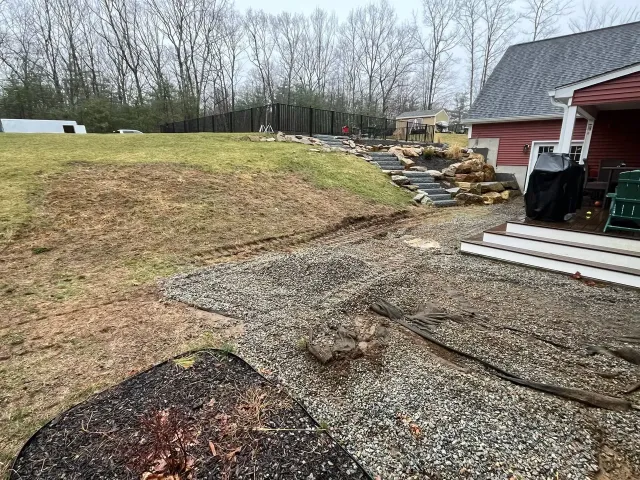 Backyard with gravel, sloped hill with steps, and a red house.