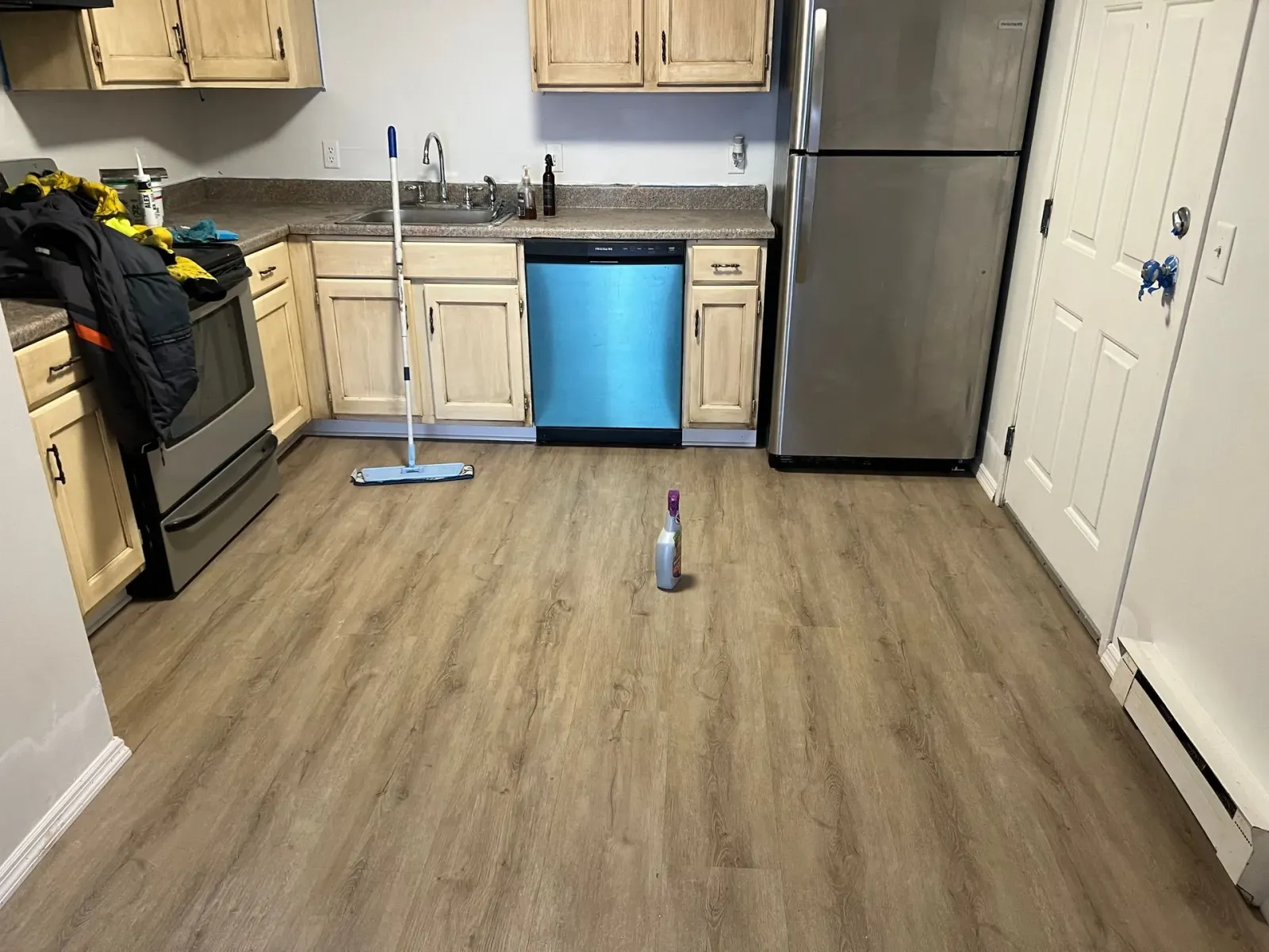 A kitchen with wooden floors , stainless steel appliances , and a mop on the floor.
