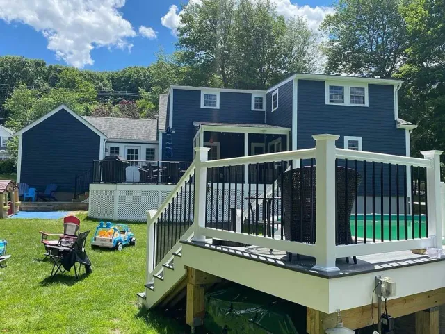 A large blue house with a white deck and a pool in the backyard.