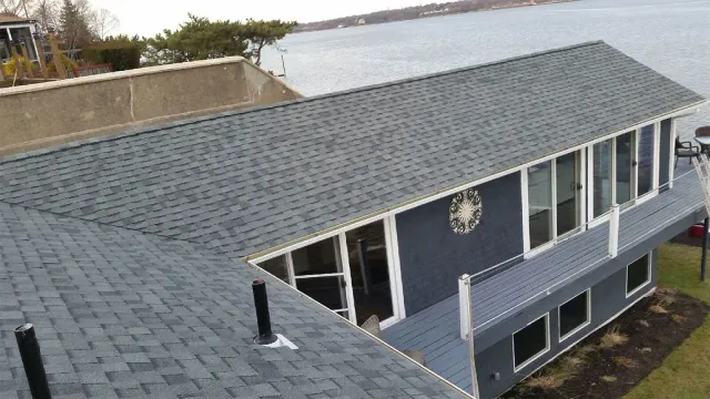 Aerial view of a gray-roofed house with a dark blue exterior and white trim near the water