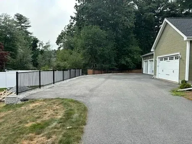 Paved driveway beside a garage and fenced yard, with trees and grass along the edge.