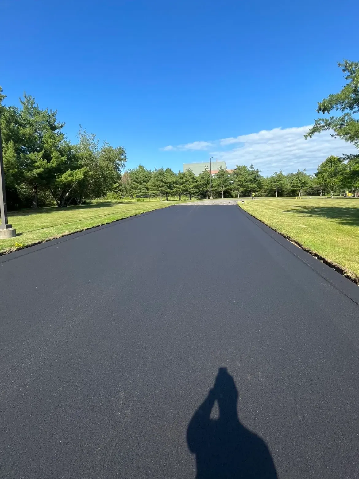 A shadow of a person is cast on a asphalt road