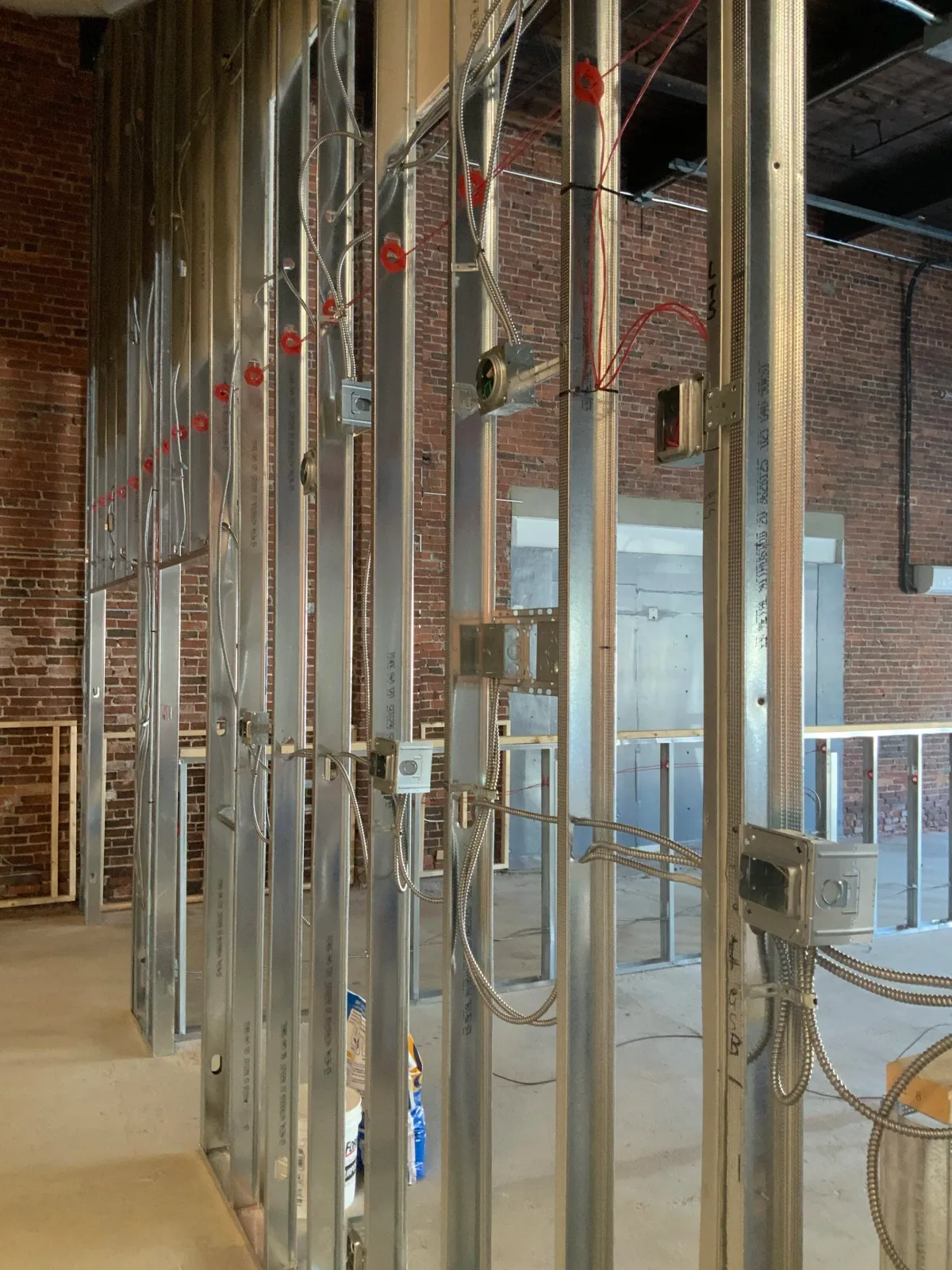 Metal stud framing with electrical wiring in a construction site with exposed brick walls.