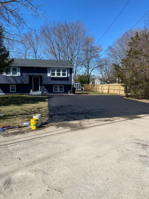 Dark blue house with a newly paved black driveway, sunny day.
