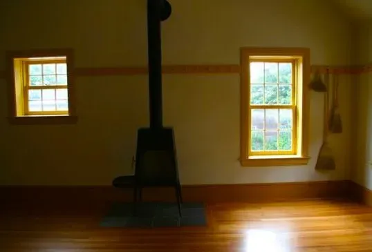 Empty room with wood floor, windows, and wood stove.