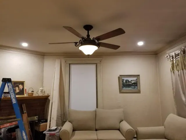 Living room with beige sofa, ceiling fan, fireplace, ladder, and framed wall art