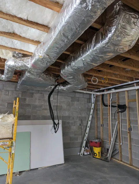 A water heater is sitting in a basement next to a stone wall.