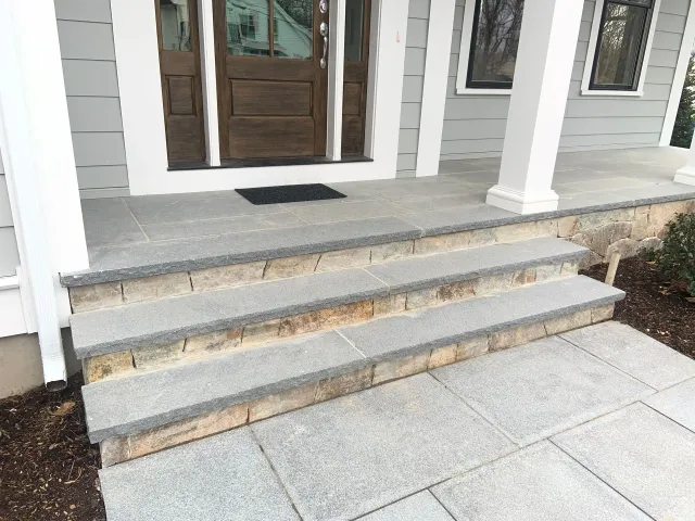 Front porch with gray stone steps, white columns, and a brown front door.